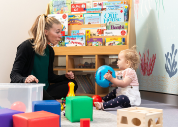 Adult playing with baby on floor as baby holds a ball and looks at them