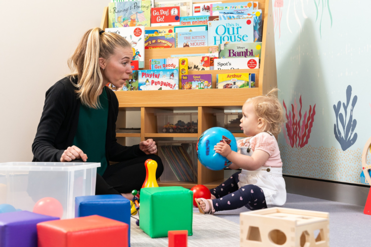 Adult playing with baby on floor as baby holds a ball and looks at them