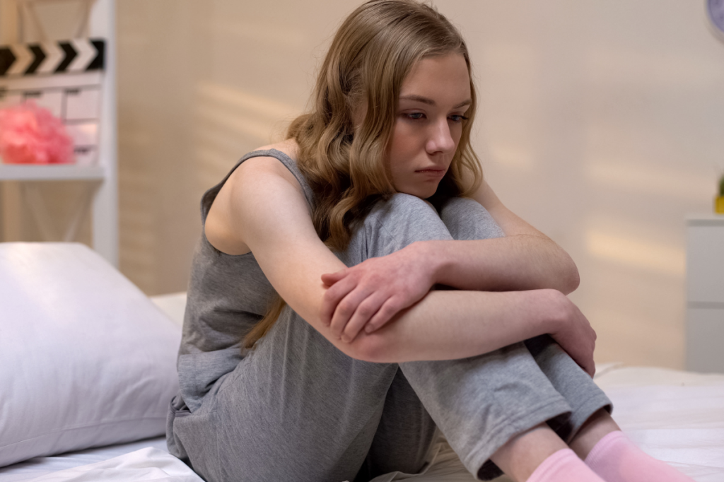 Sad girl sitting on bed, looking sad.
