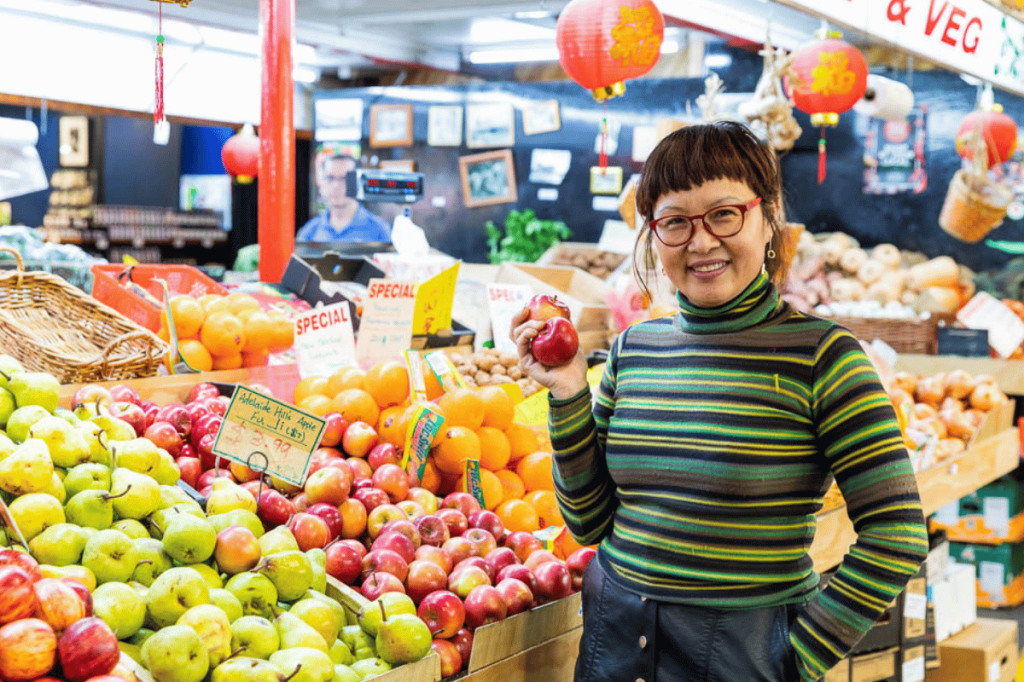 Woman holding an apple at a fruit and vegetable stall inside Adelaide Central Market