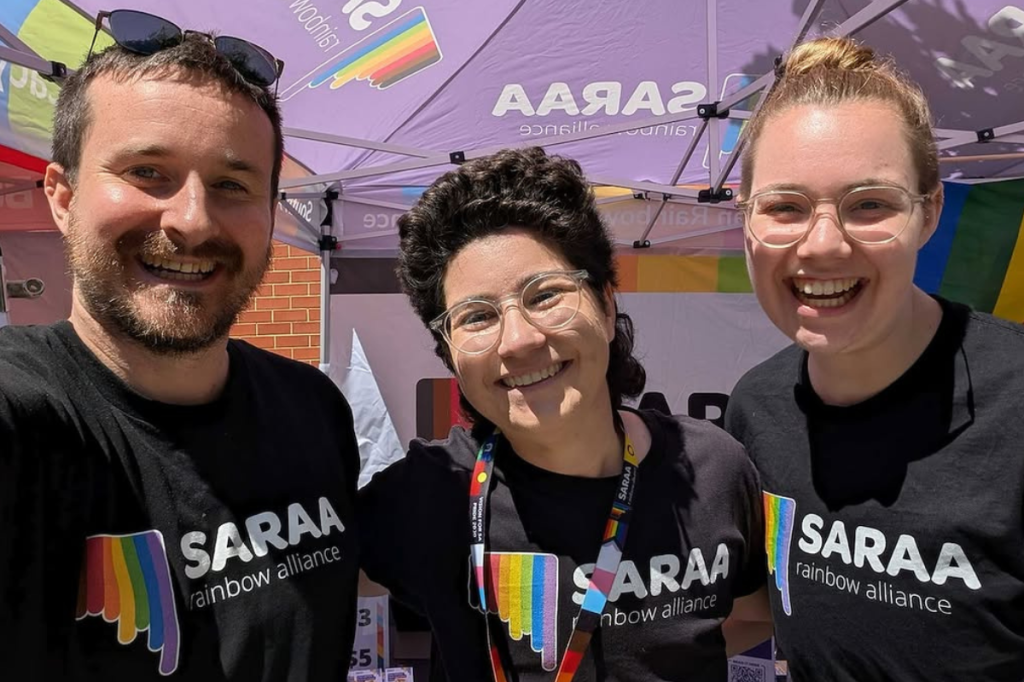 Varo Lee with other South Australian Rainbow Advocacy Alliance staff members smiling at an outdoor event.
