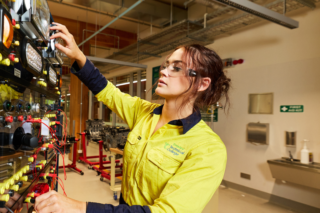 A young woman in a tradie's uniform and safety goggles at work on site.