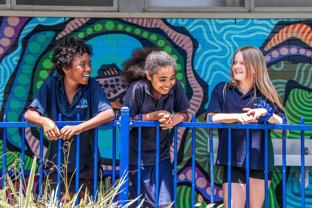 Three South Australian kids at a public school laughing and talking together.