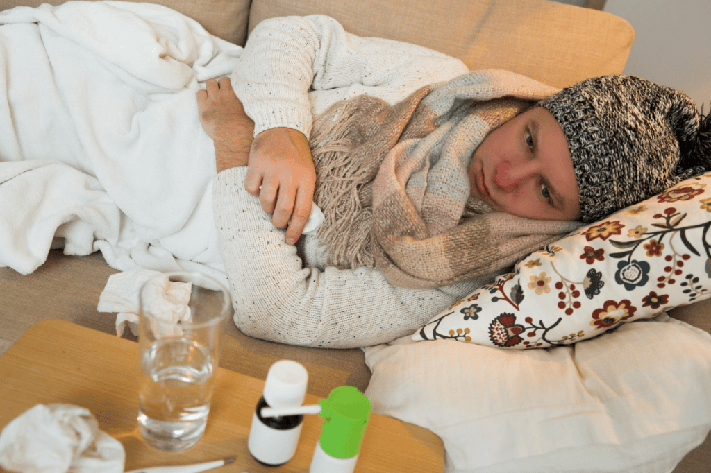 Sick man with tissues and medicine, lying on sofa.
