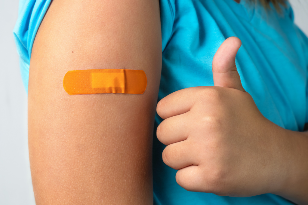 Woman with bandaid on her arm, giving the thumbs up.