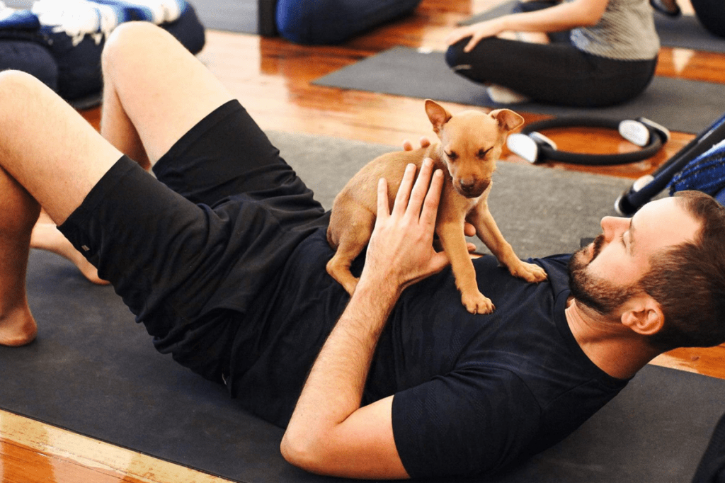 A man on a yoga mat cuddling a puppy